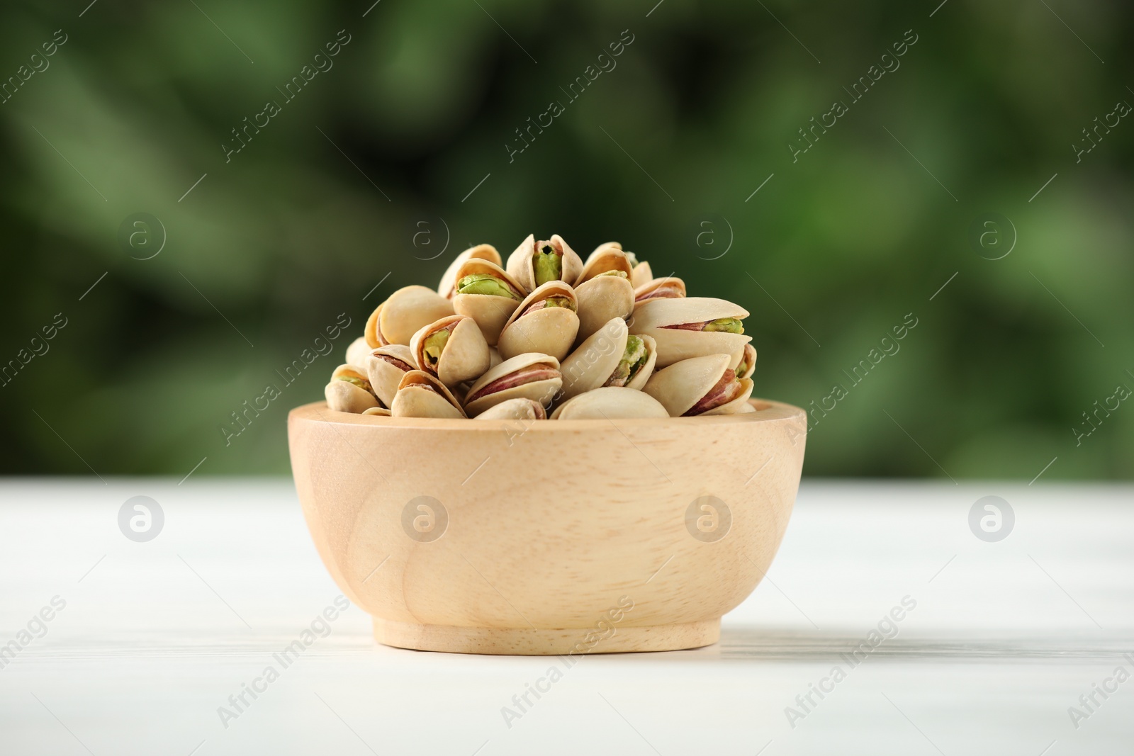 Photo of Tasty pistachios in bowl on white wooden table against blurred background, closeup