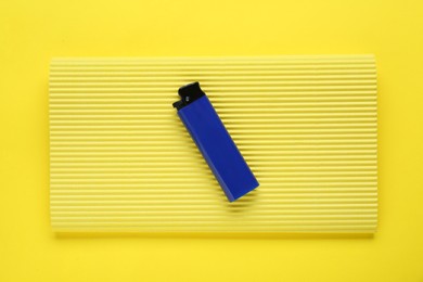 Stylish small pocket lighter with corrugated fiberboard on yellow background, top view