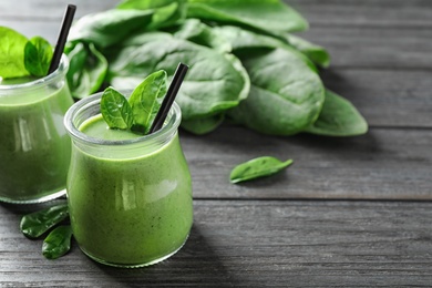 Jars of healthy green smoothie with fresh spinach on grey wooden table. Space for text