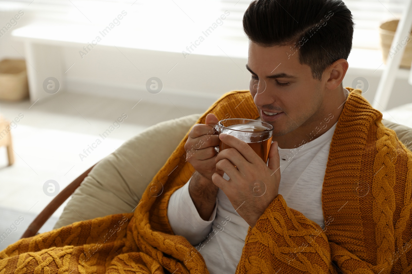 Photo of Man covered with warm orange plaid enjoying hot drink at home