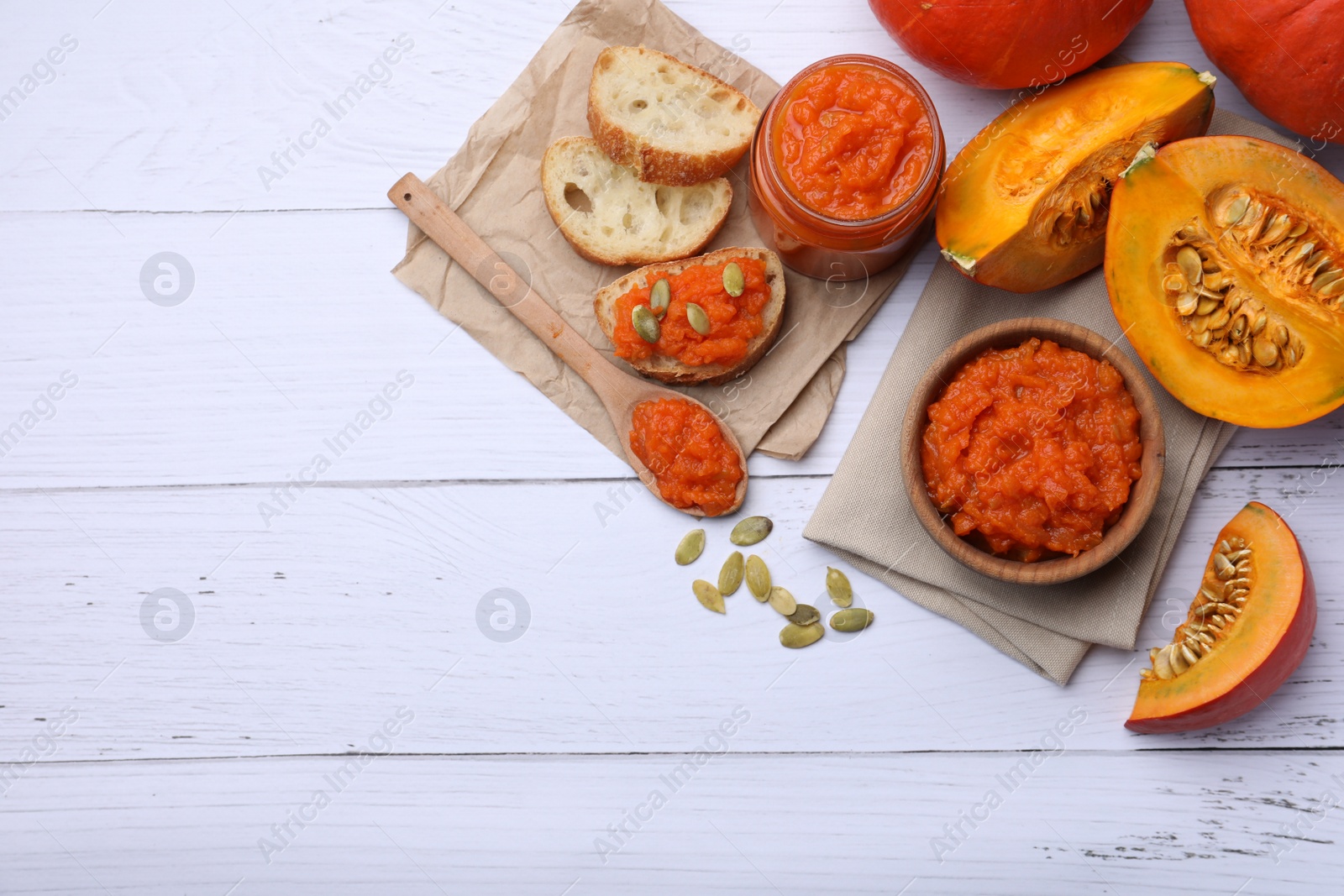 Photo of Delicious pumpkin jam and fresh pumpkin on white wooden table, flat lay. Space for text