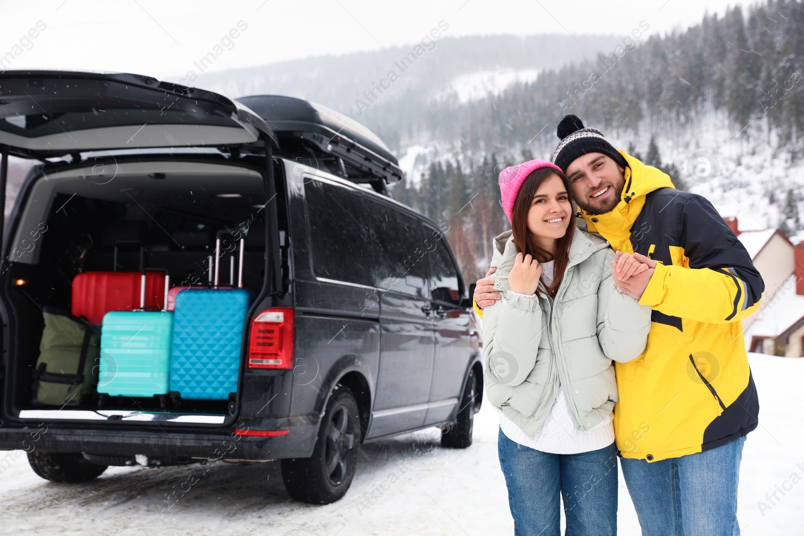 Photo of Happy couple near car with open trunk on snowy road. Winter vacation