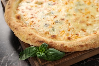 Photo of Delicious cheese pizza and basil on black marble table, closeup