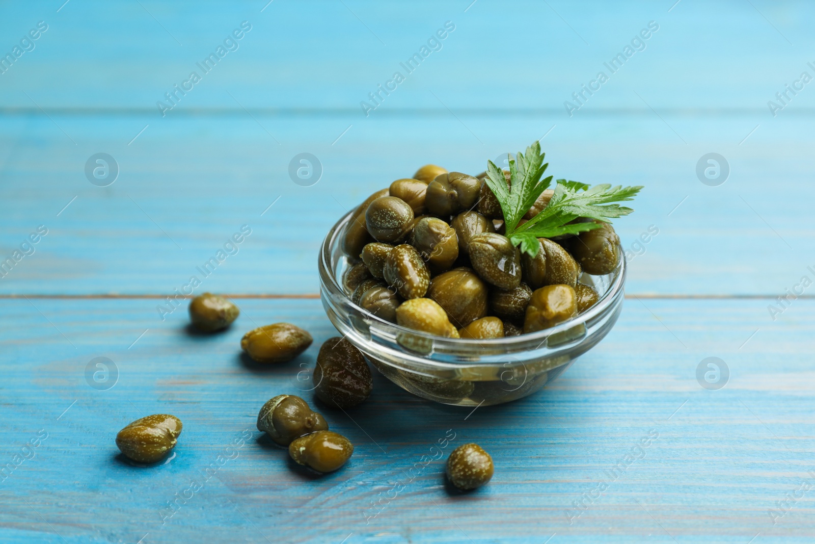 Photo of Tasty capers and parsley on light blue wooden table