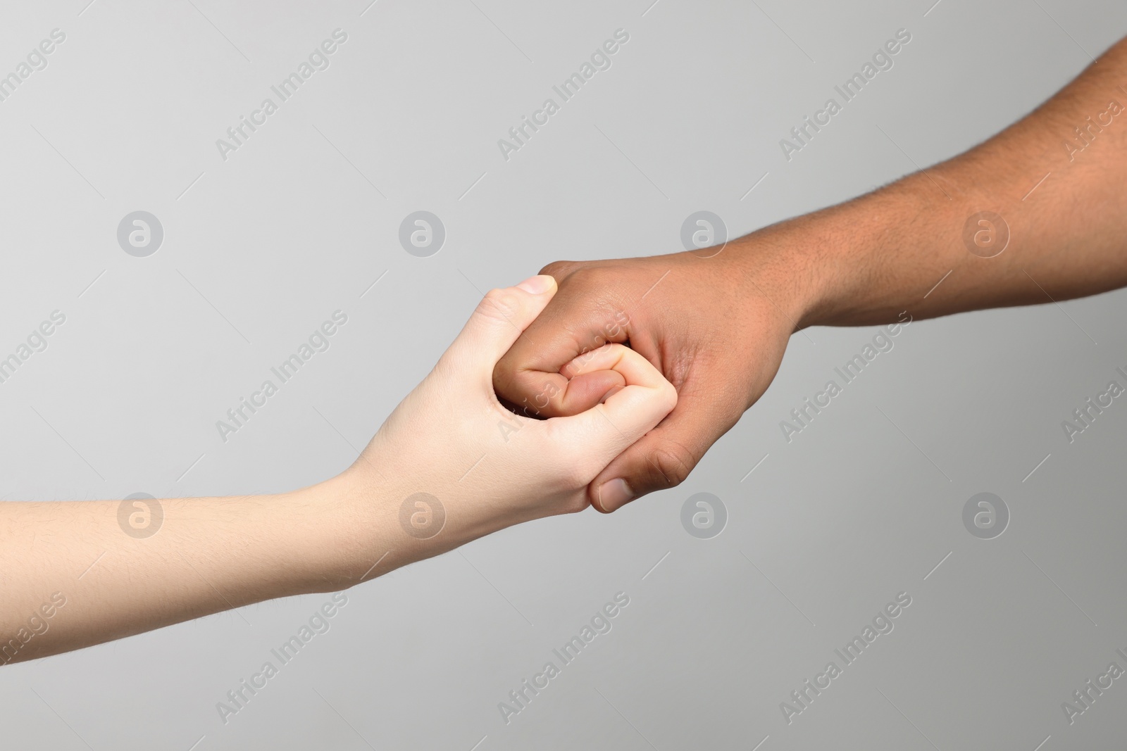 Photo of International relationships. People strongly joining hands on light grey background, closeup