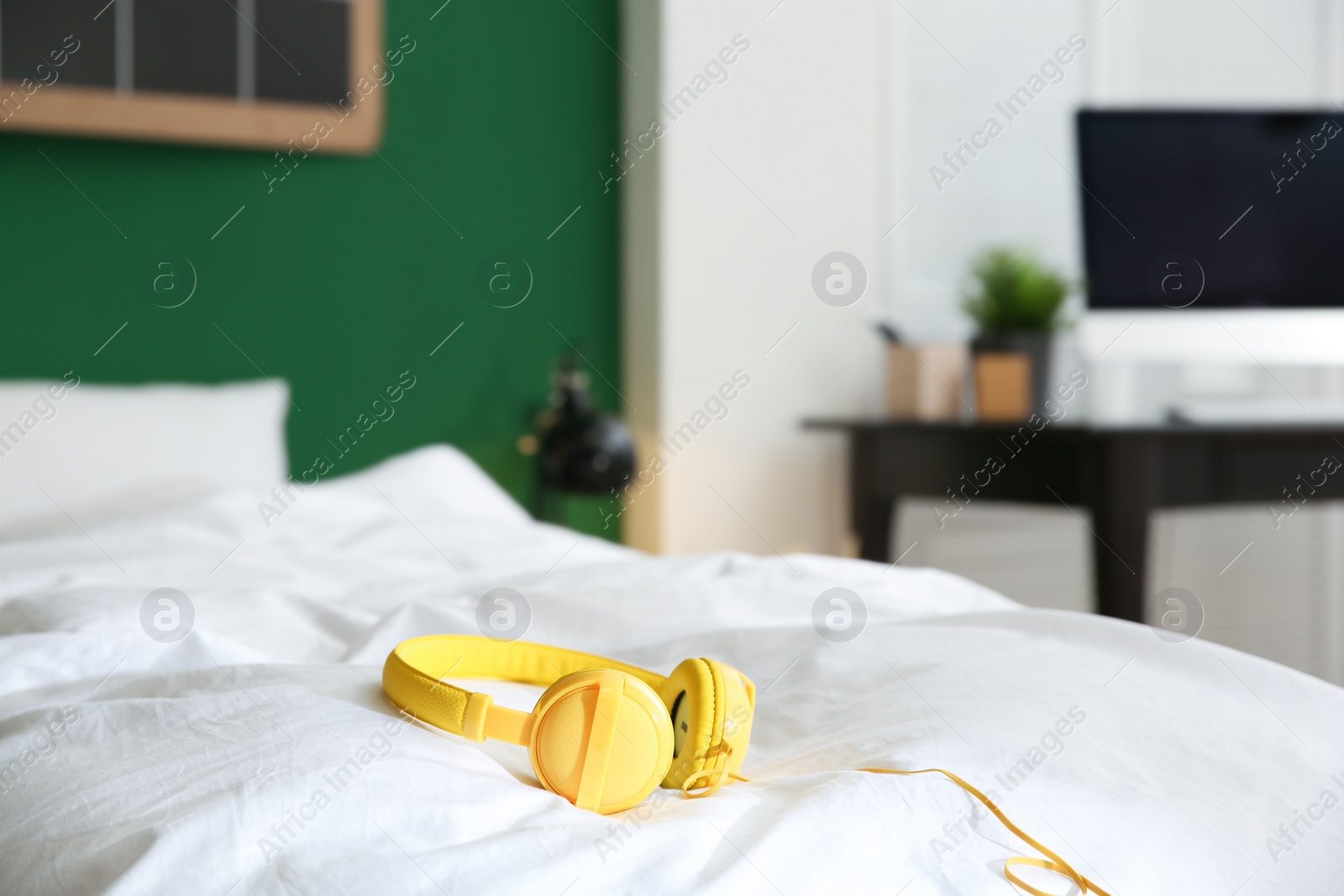 Photo of Stylish modern headphones with earmuffs on bed against blurred background, space for text