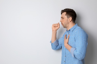 Photo of Young man coughing on light background