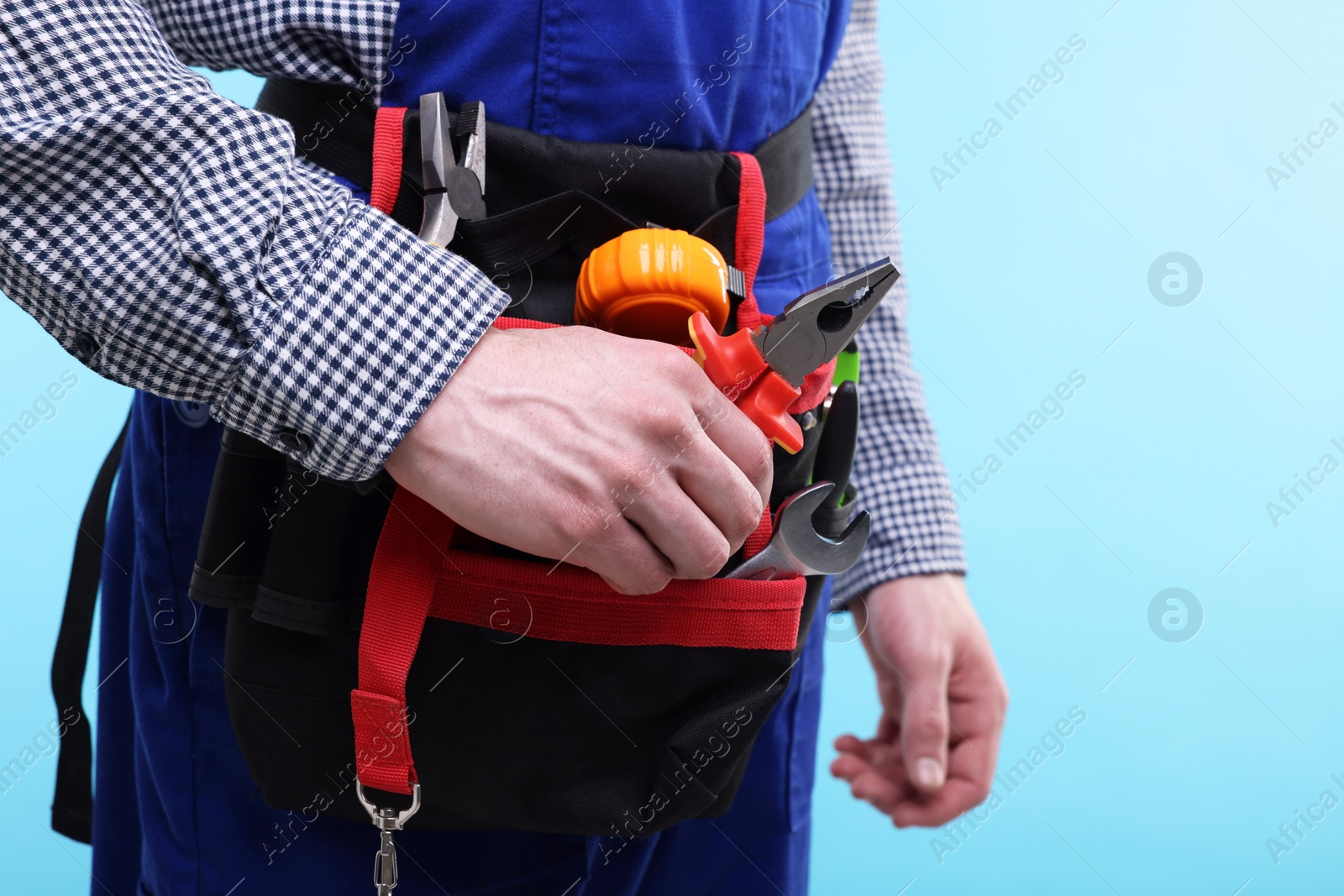 Photo of Young man with pliers and other tools in bag on light blue background, closeup