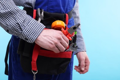 Photo of Young man with pliers and other tools in bag on light blue background, closeup