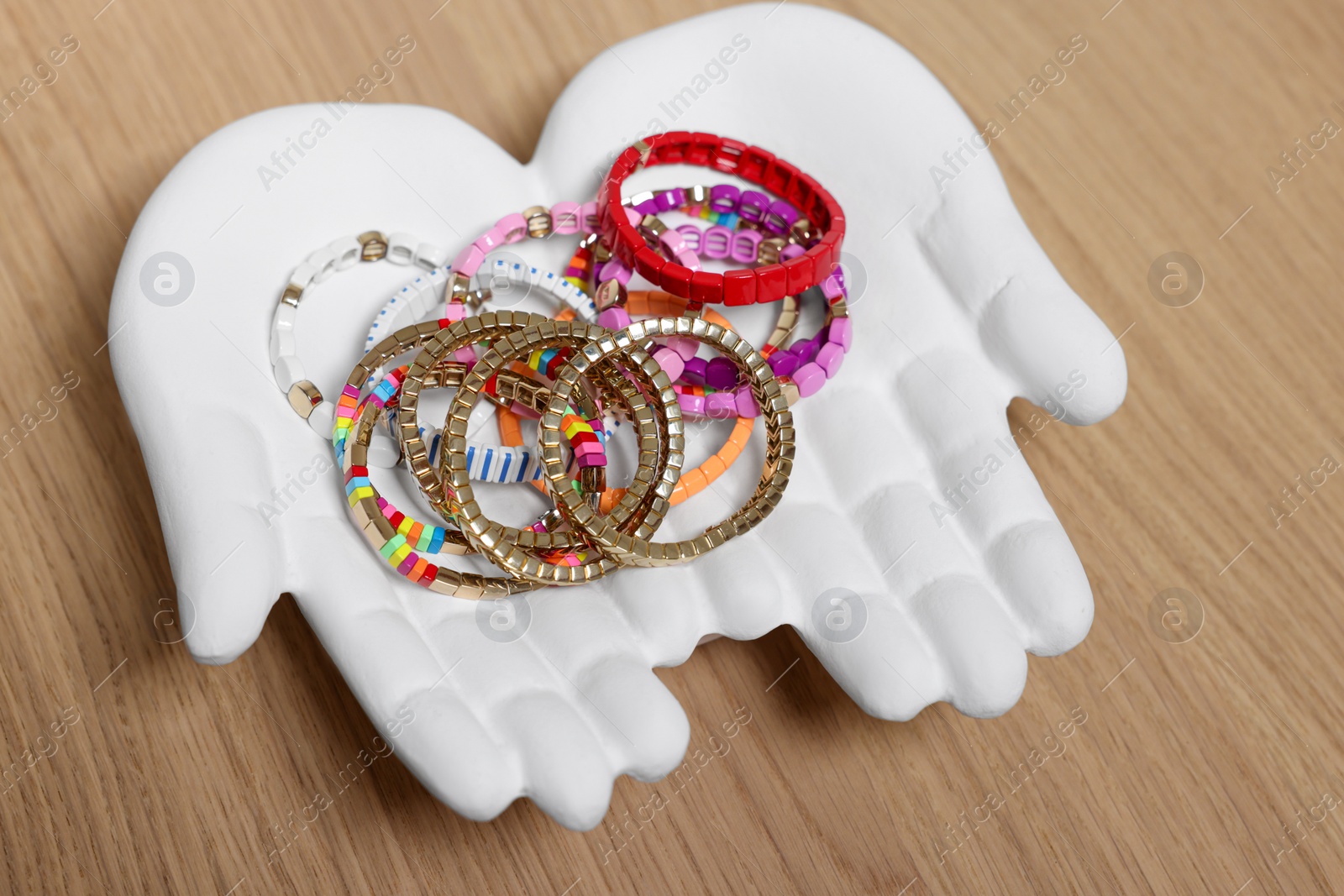 Photo of Ceramic hand stand with many different bracelets on wooden table