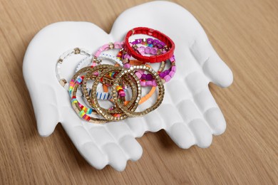 Ceramic hand stand with many different bracelets on wooden table