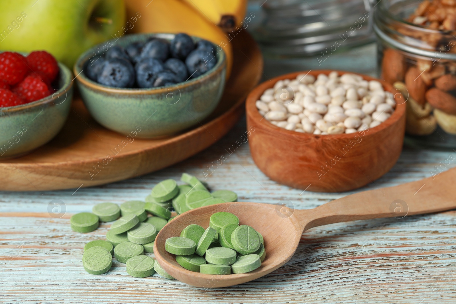 Photo of Spoon with pills and foodstuff on wooden table, closeup. Prebiotic supplements