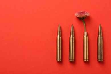 Bullets and cartridge case with beautiful flower on red background, flat lay. Space for text