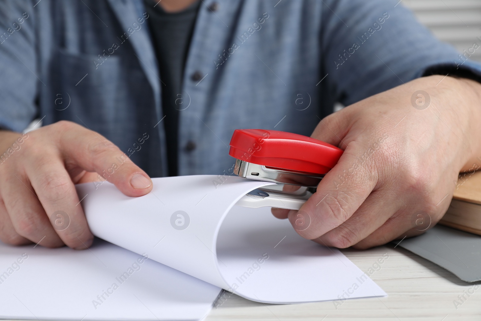 Photo of Man with papers using stapler at white wooden table, closeup