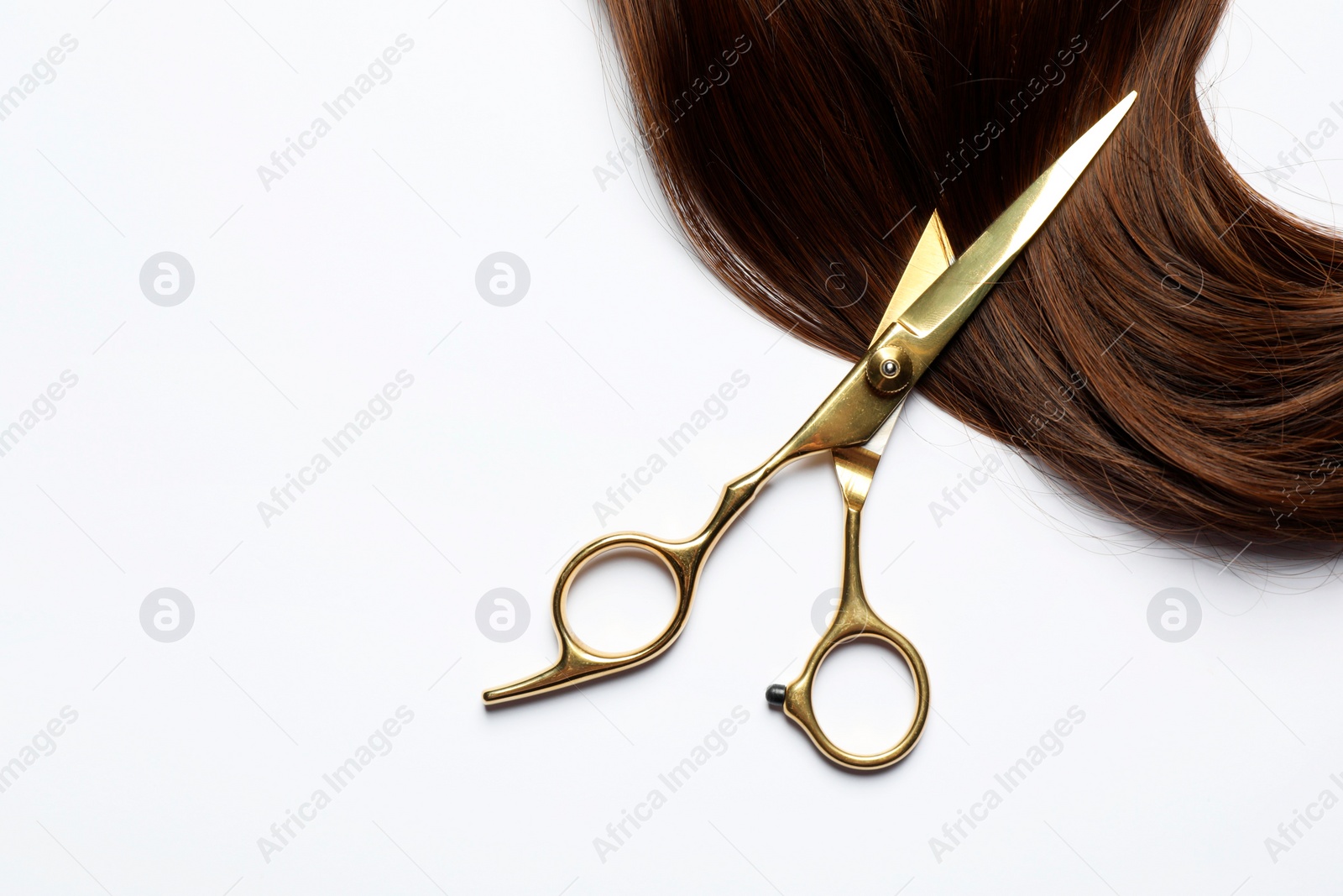 Photo of Professional hairdresser scissors with brown hair strand on white background, top view