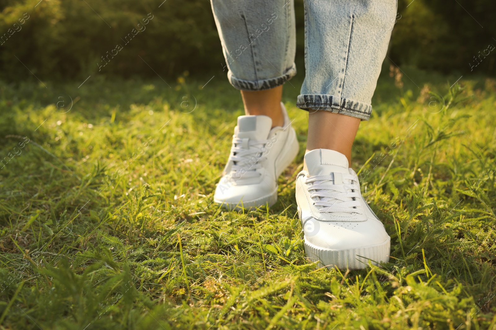 Photo of Woman in jeans and white shoes walking on green grass, closeup. Space for text