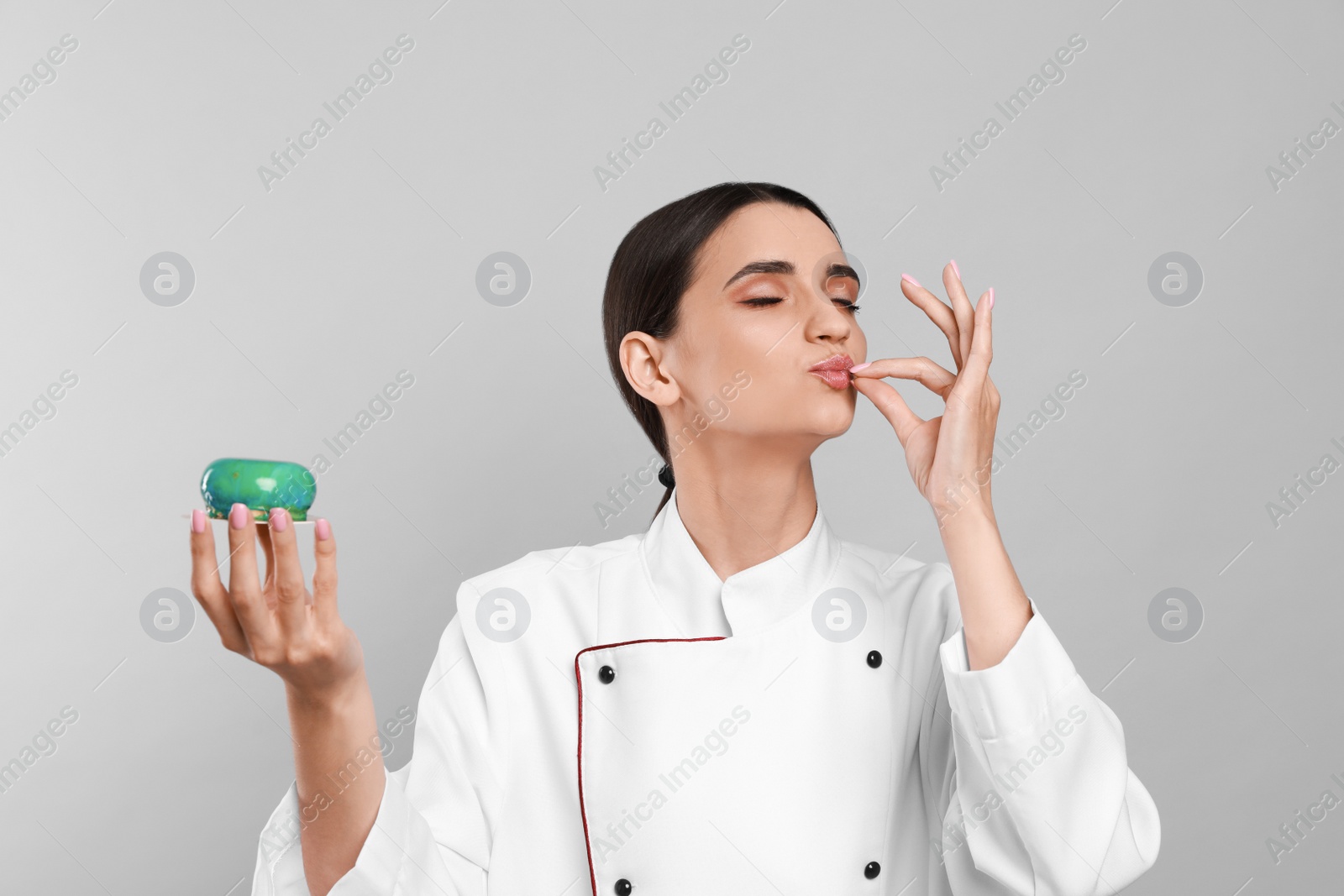 Photo of Professional confectioner in uniform with cake showing delicious gesture on light grey background