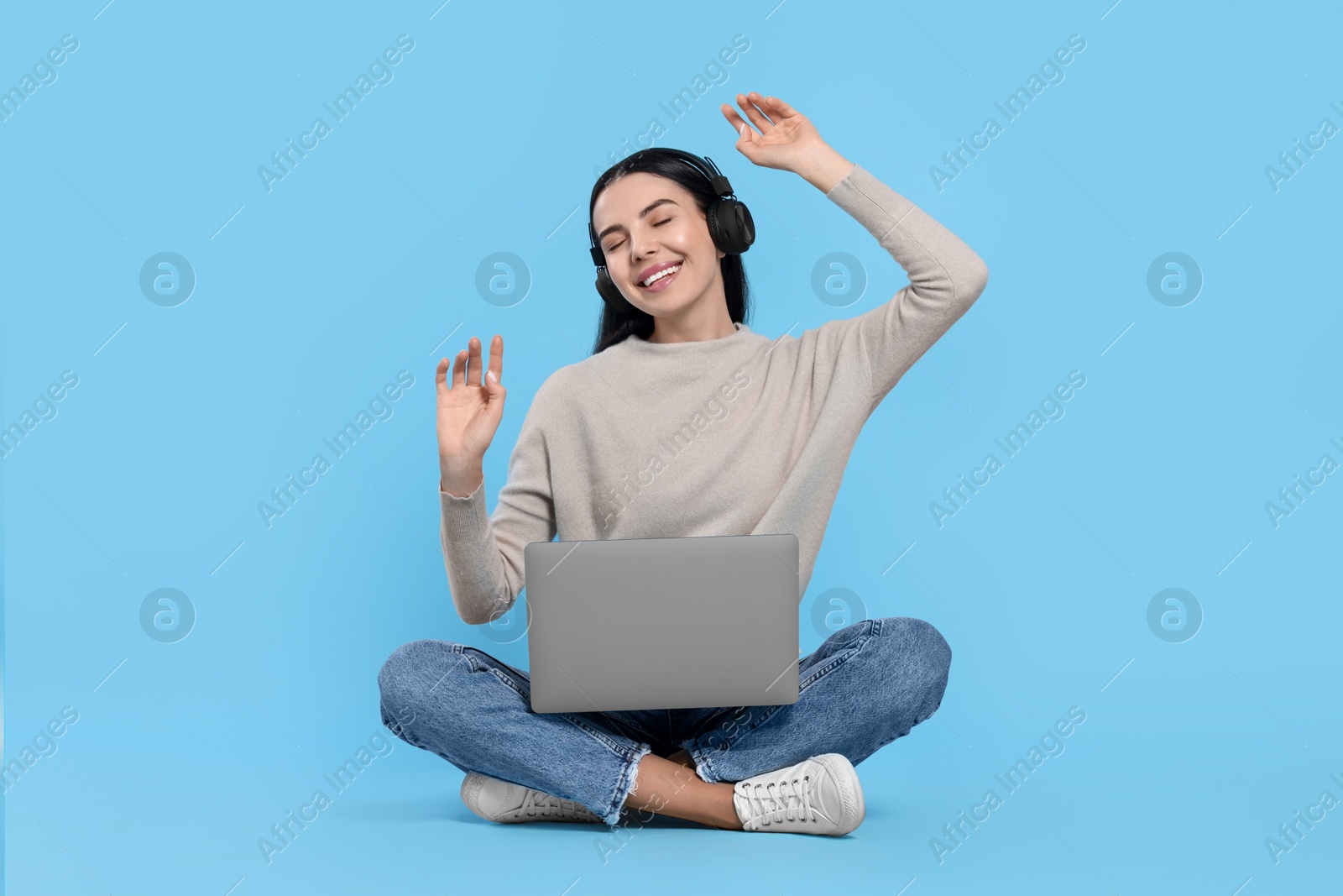 Photo of Happy woman with laptop listening to music in headphones on light blue background