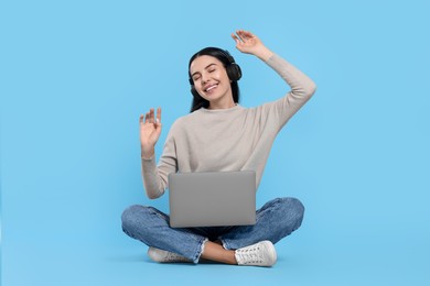 Photo of Happy woman with laptop listening to music in headphones on light blue background