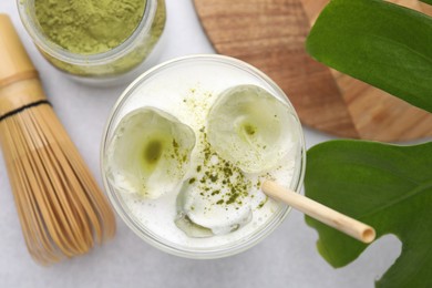 Photo of Glass of tasty iced matcha latte, leaf, powder and bamboo whisk on white table