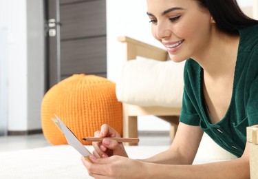 Happy woman writing message in greeting card on carpet in living room