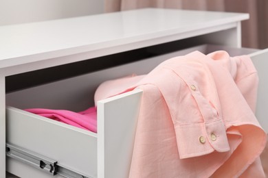 Photo of Pink shirt on white chest of drawers indoors, closeup