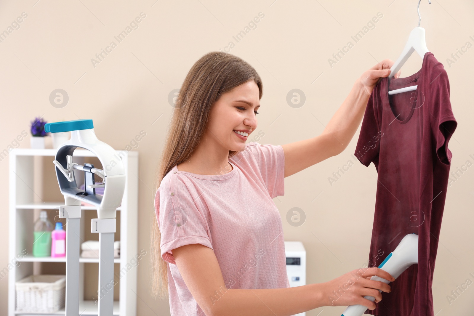 Photo of Young woman steaming her clothes at home