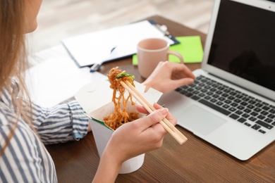 Photo of Office employee using laptop while having noodles for lunch at workplace, closeup. Food delivery