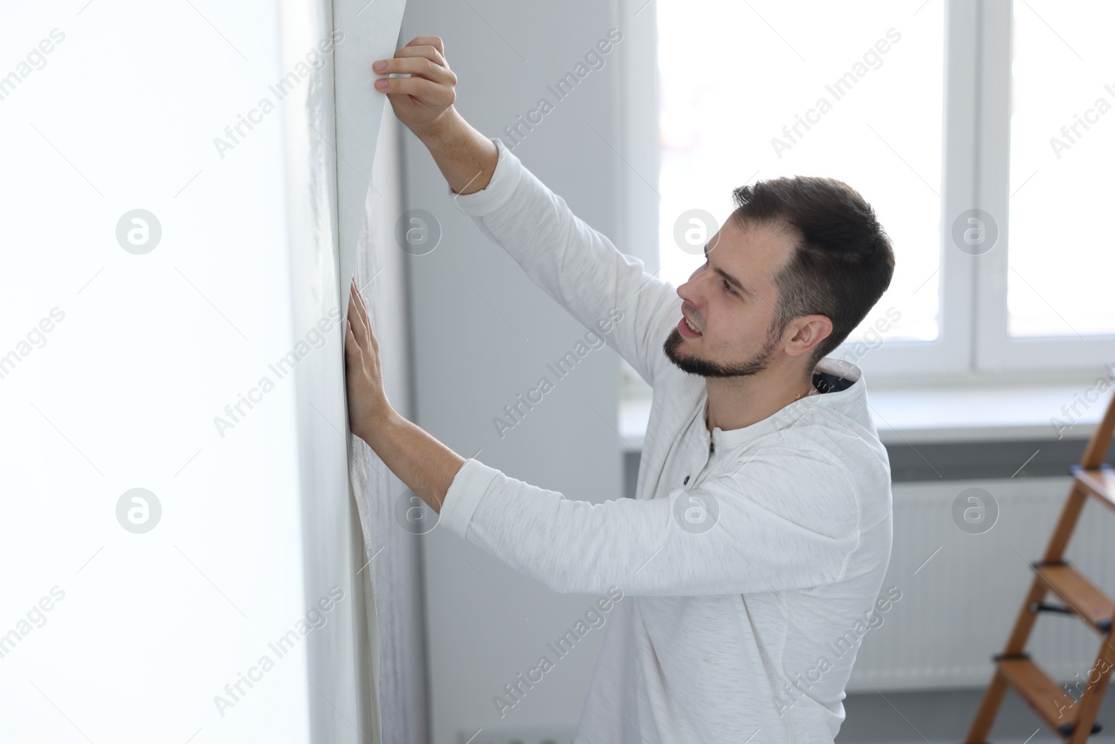 Photo of Man hanging stylish gray wallpaper in room