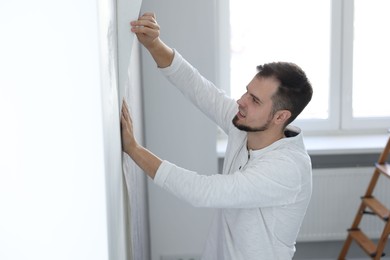 Man hanging stylish gray wallpaper in room