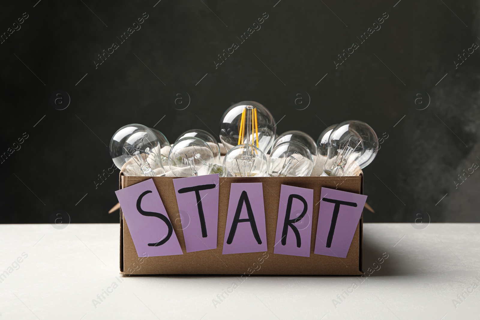 Photo of Vintage and modern lamp bulbs in box with word Start on white table