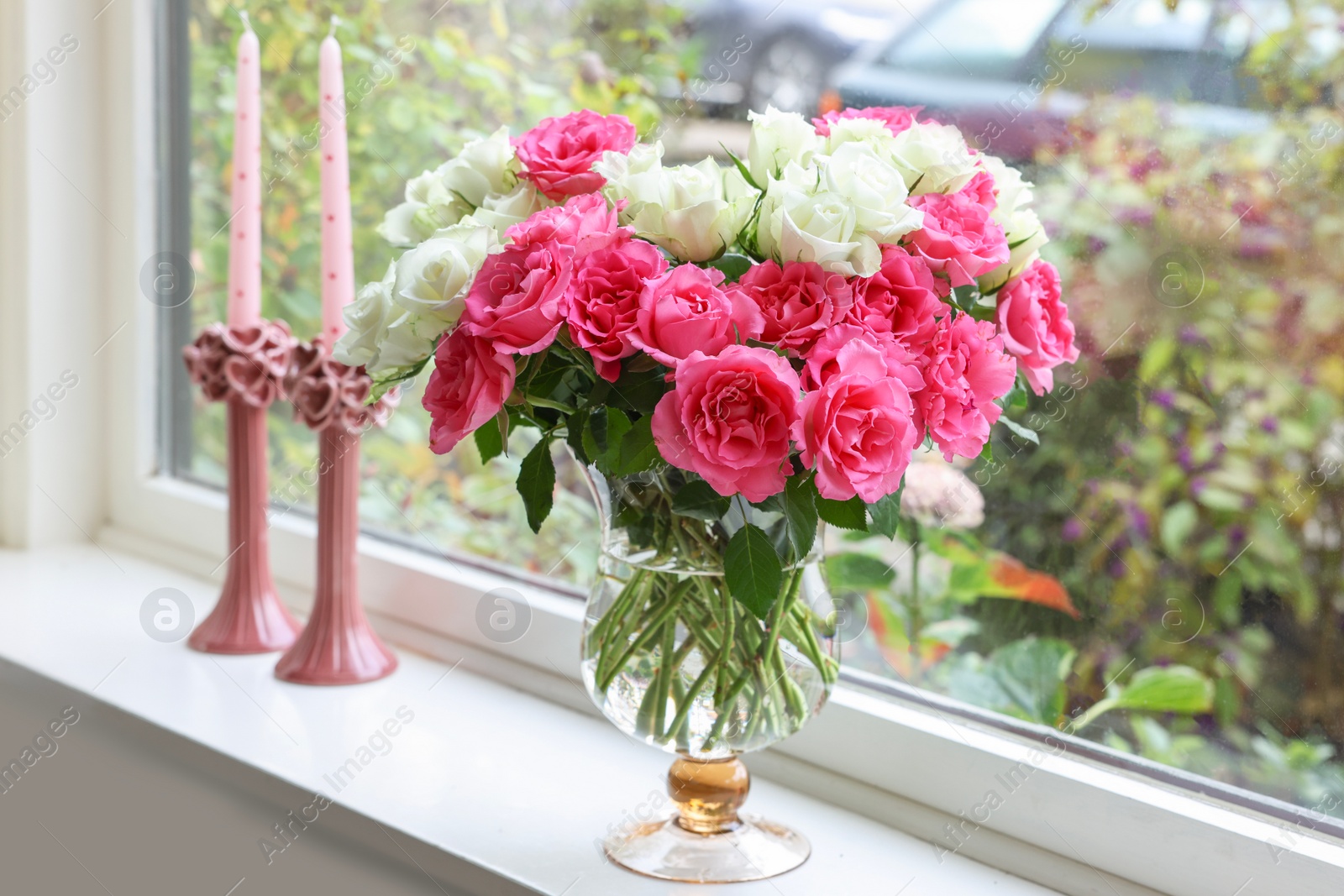 Photo of Vase with beautiful bouquet of roses and candles on windowsill indoors