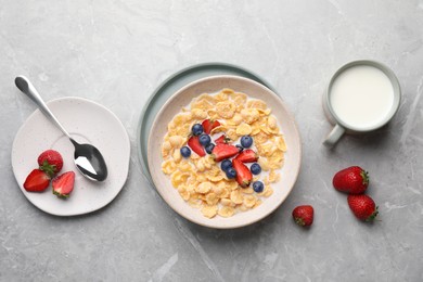 Photo of Bowl of tasty crispy corn flakes with milk and berries on light grey table, flat lay