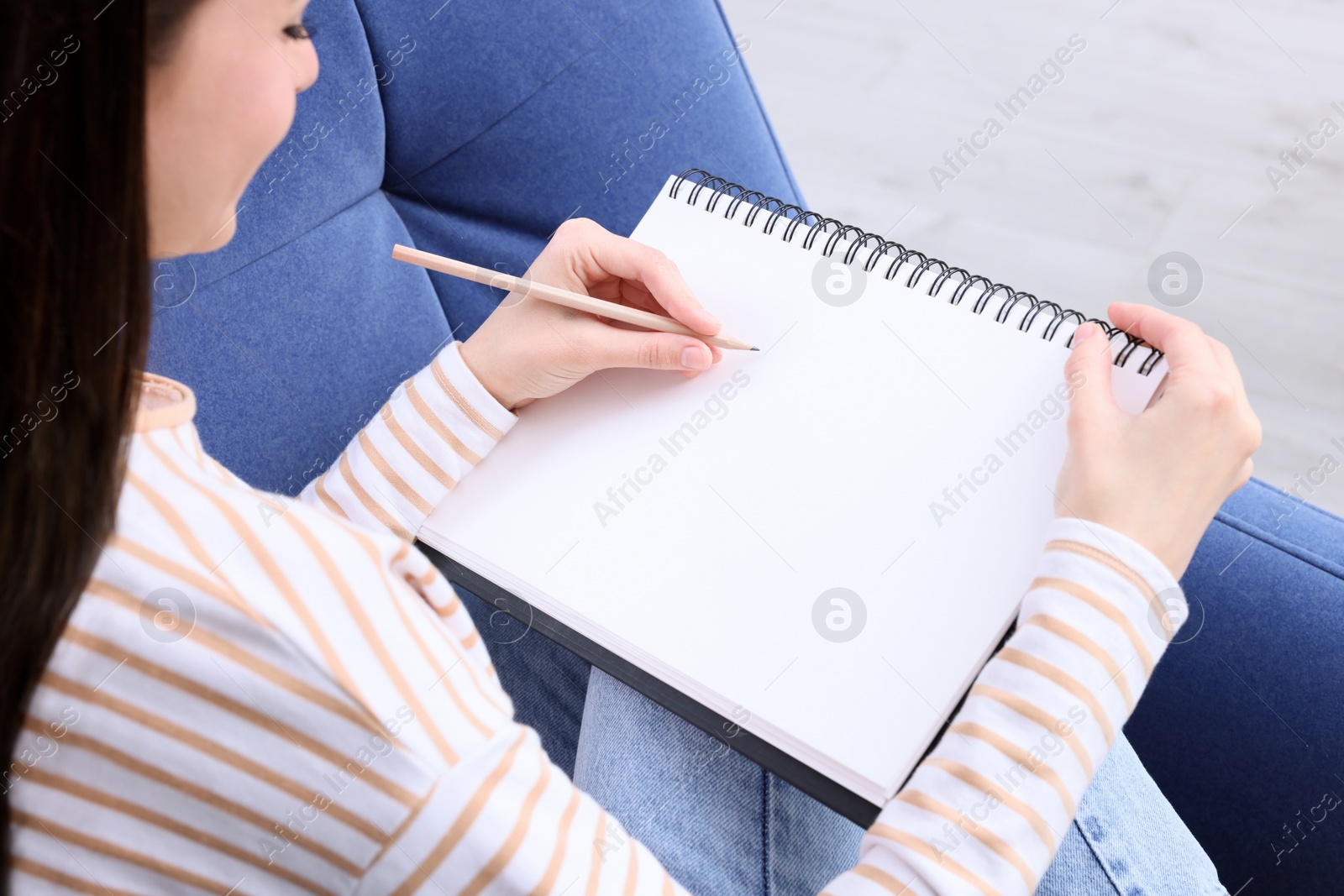 Photo of Young woman drawing in sketchbook indoors, closeup