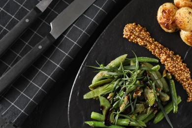 Photo of Delicious salad with tarragon, mustard and grilled potatoes on black table, flat lay