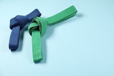 Photo of Colorful karate belts on light blue background, space for text