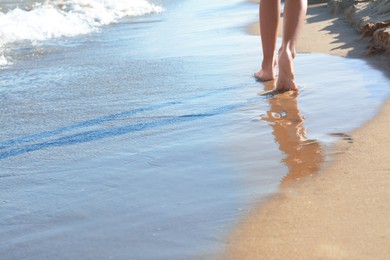 Woman walking on sandy beach near sea, closeup. Space for text