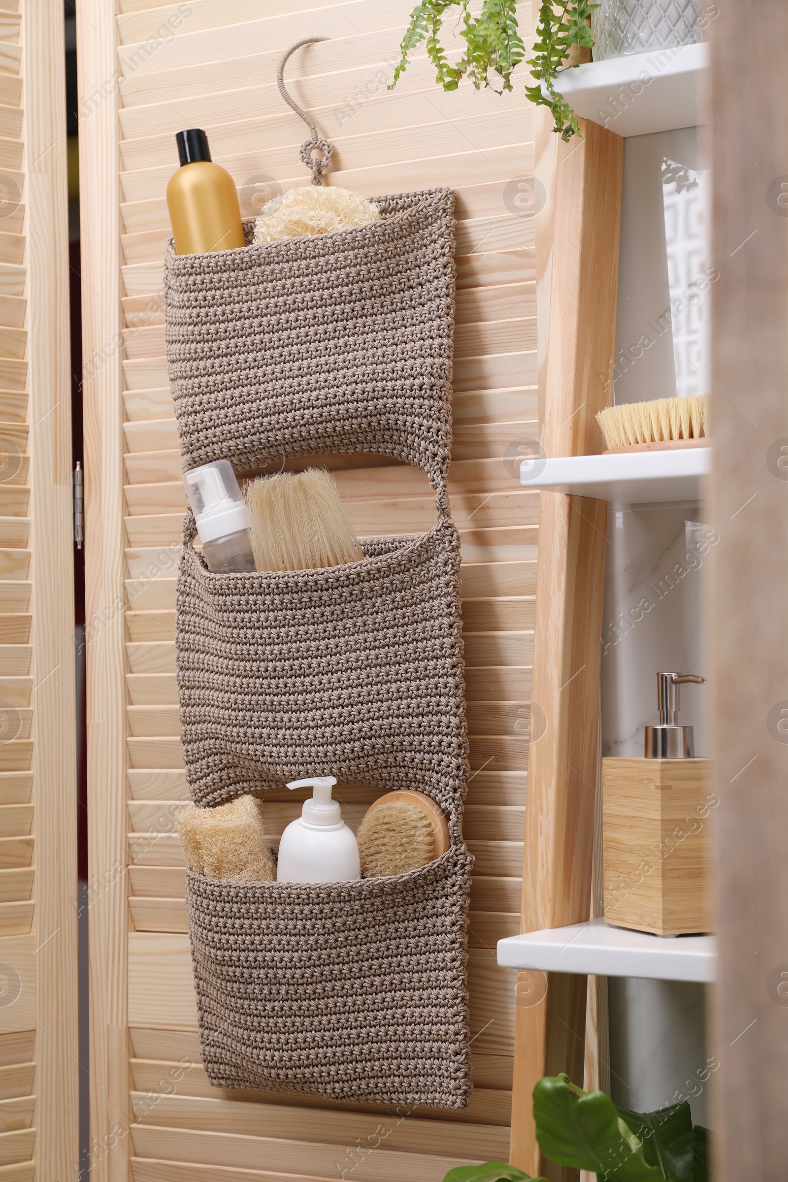 Photo of Storage with essentials hanging on wooden folding screen in bathroom. Stylish accessory