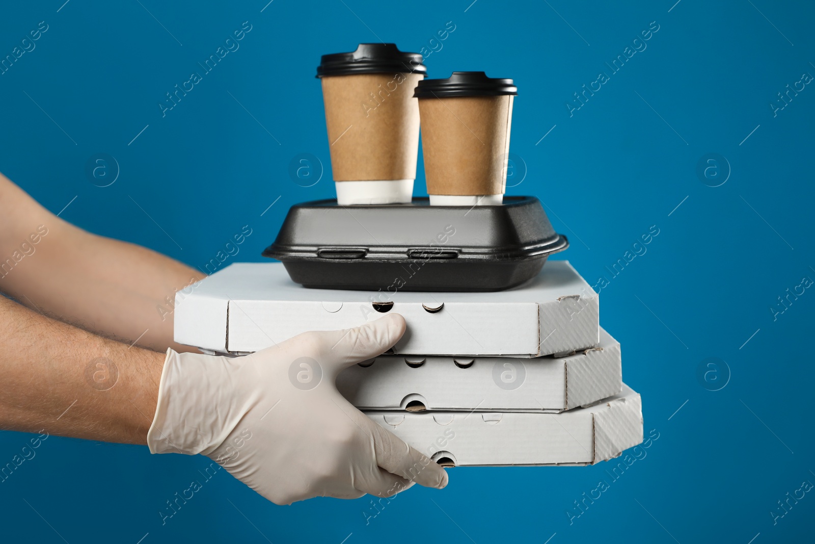 Photo of Courier in protective gloves holding order on blue background, closeup. Food delivery service during coronavirus quarantine