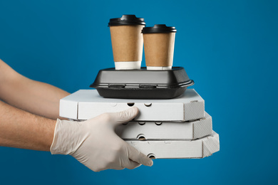 Courier in protective gloves holding order on blue background, closeup. Food delivery service during coronavirus quarantine