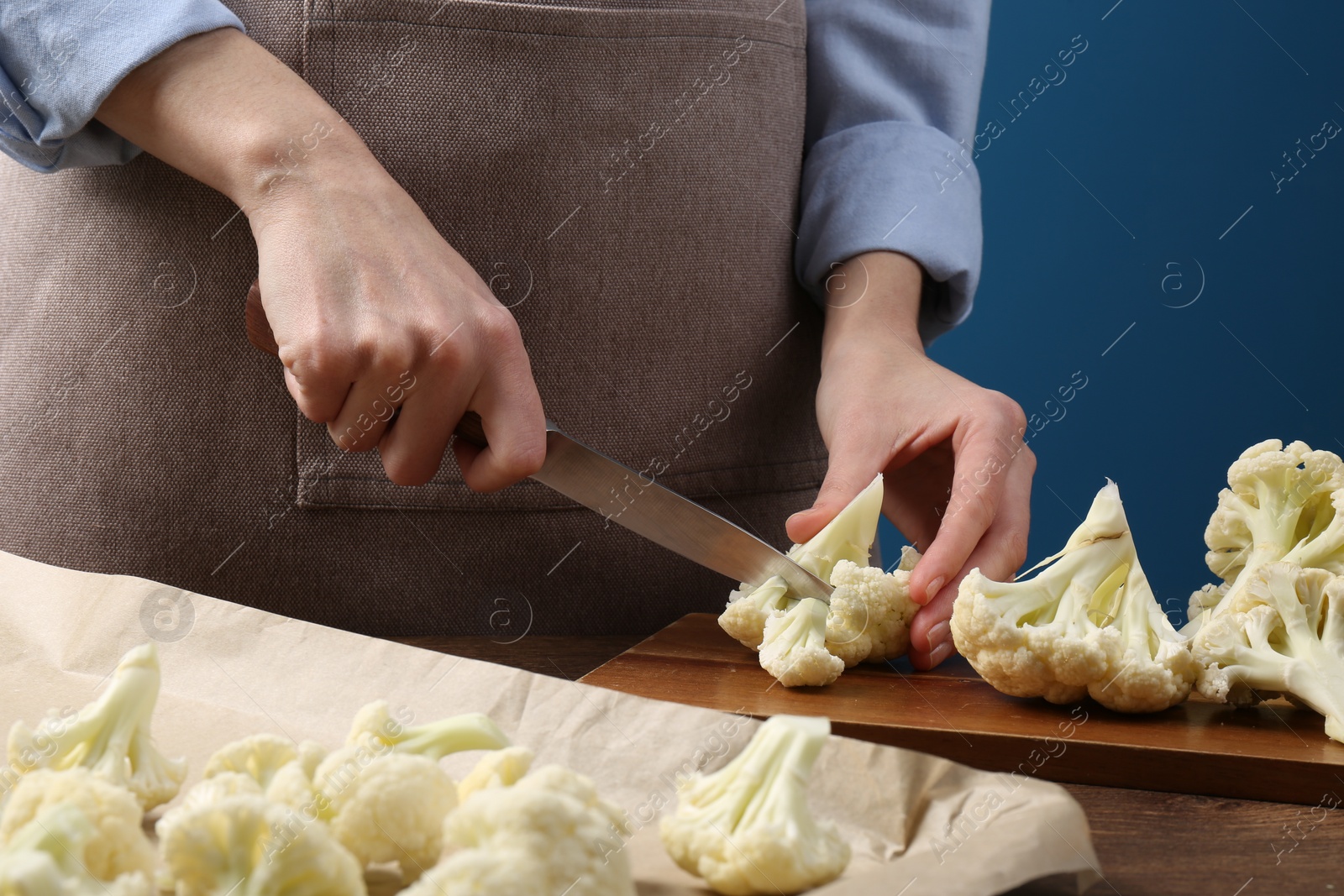 Photo of Woman cutting fresh cauliflower at wooden table, closeup