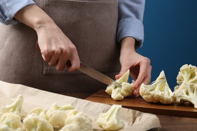 Photo of Woman cutting fresh cauliflower at wooden table, closeup