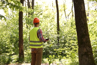 Photo of Forester with laptop examining plants in forest, back view