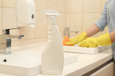 Photo of Woman cleaning sink in bathroom, focus on bottle of detergent