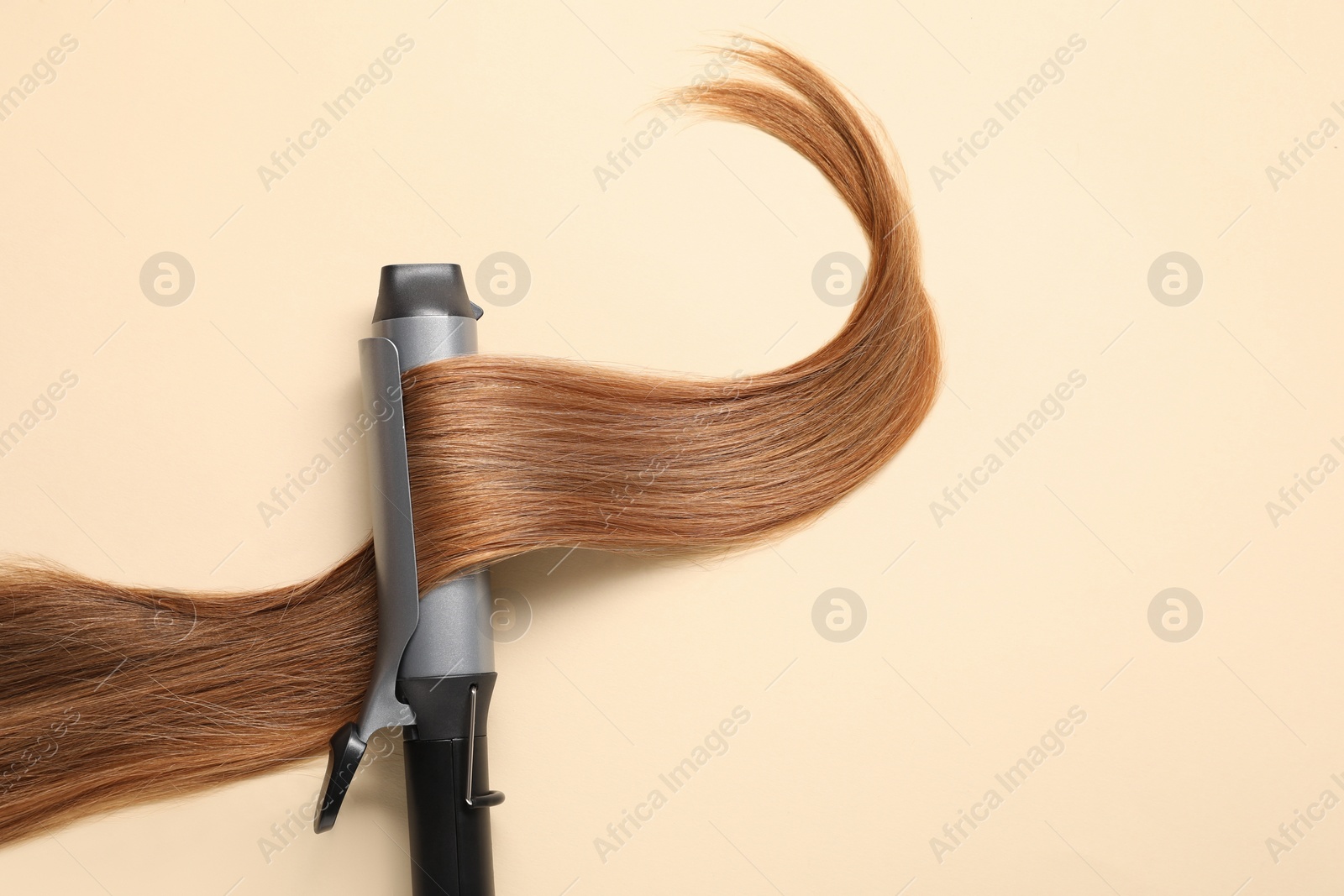 Photo of Curling iron with hair lock on beige background, top view. Space for text