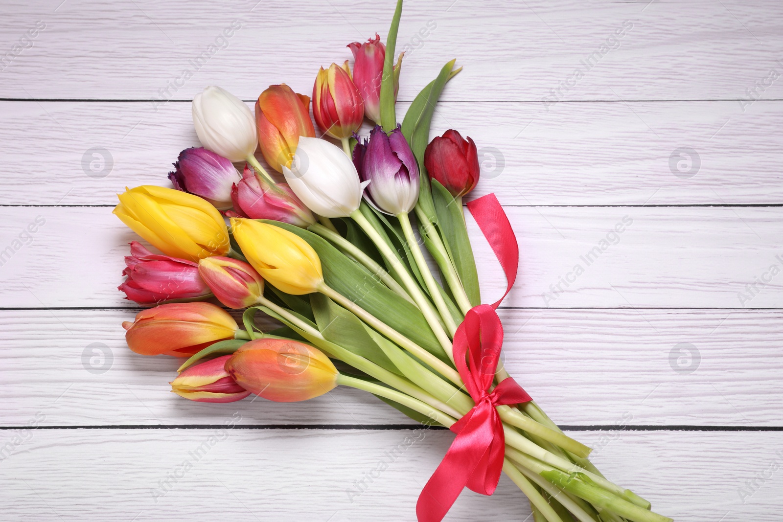 Photo of Bouquet of beautiful colorful tulip flowers tied with red ribbon on white wooden table, top view