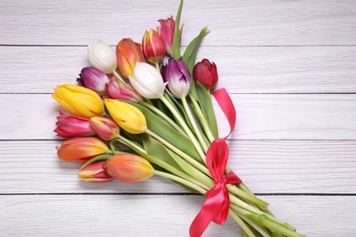 Bouquet of beautiful colorful tulip flowers tied with red ribbon on white wooden table, top view