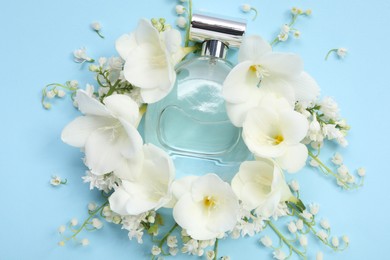 Photo of Luxury perfume and floral decor on light blue background, flat lay