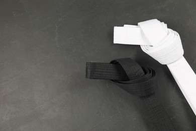 Photo of White and black karate belts on gray background, flat lay. Space for text