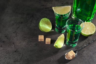 Absinthe in shot glasses, spoon, lime and brown sugar cubes on gray textured table, space for text. Alcoholic drink